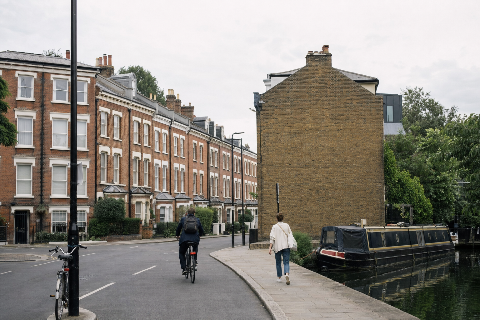 A cyclist and pedestrian pass by terraced houses alongside a canal with a narrowboat moored.