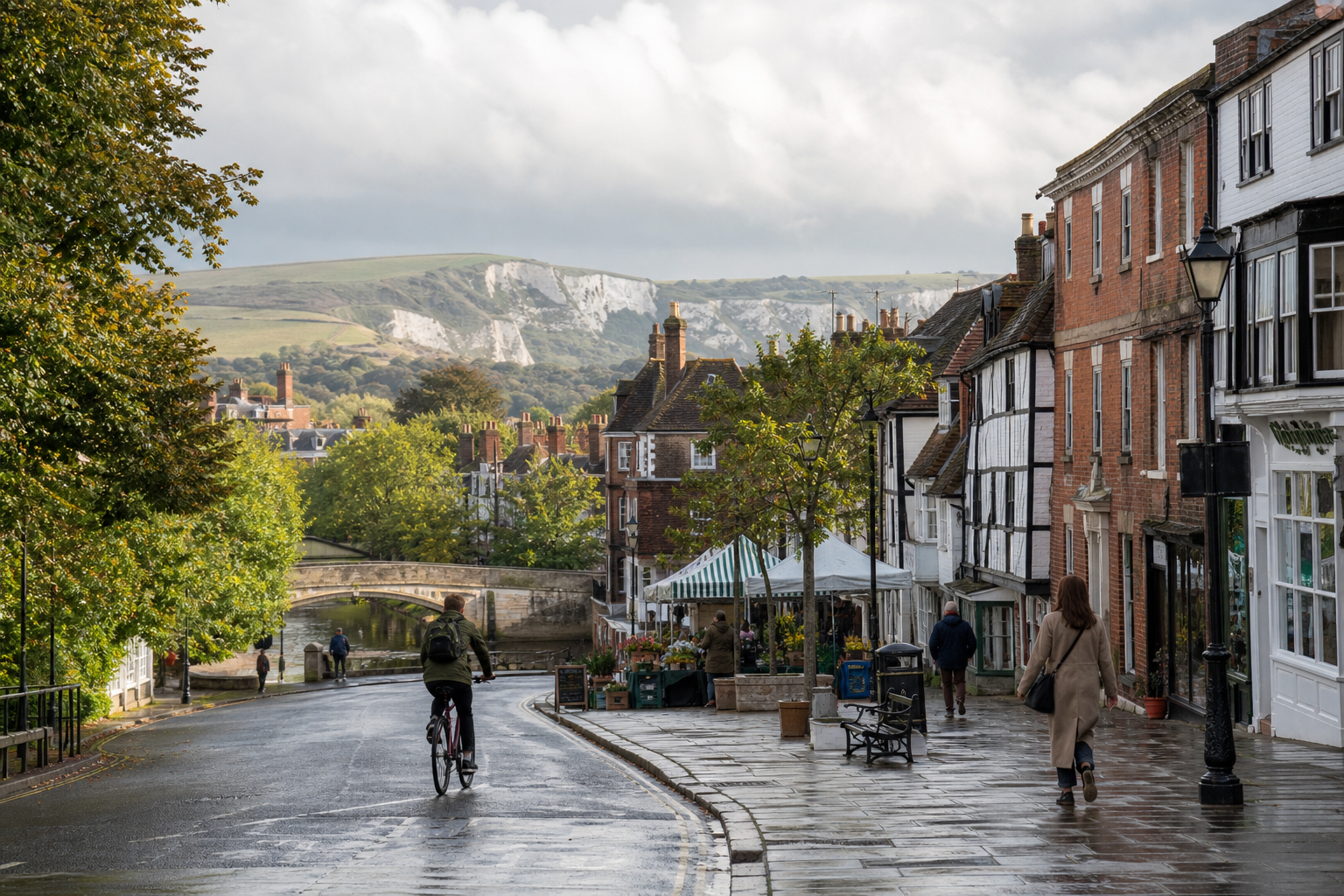 A cyclist and pedestrians on a quaint street with colorful buildings and a distant view of rolling hills.