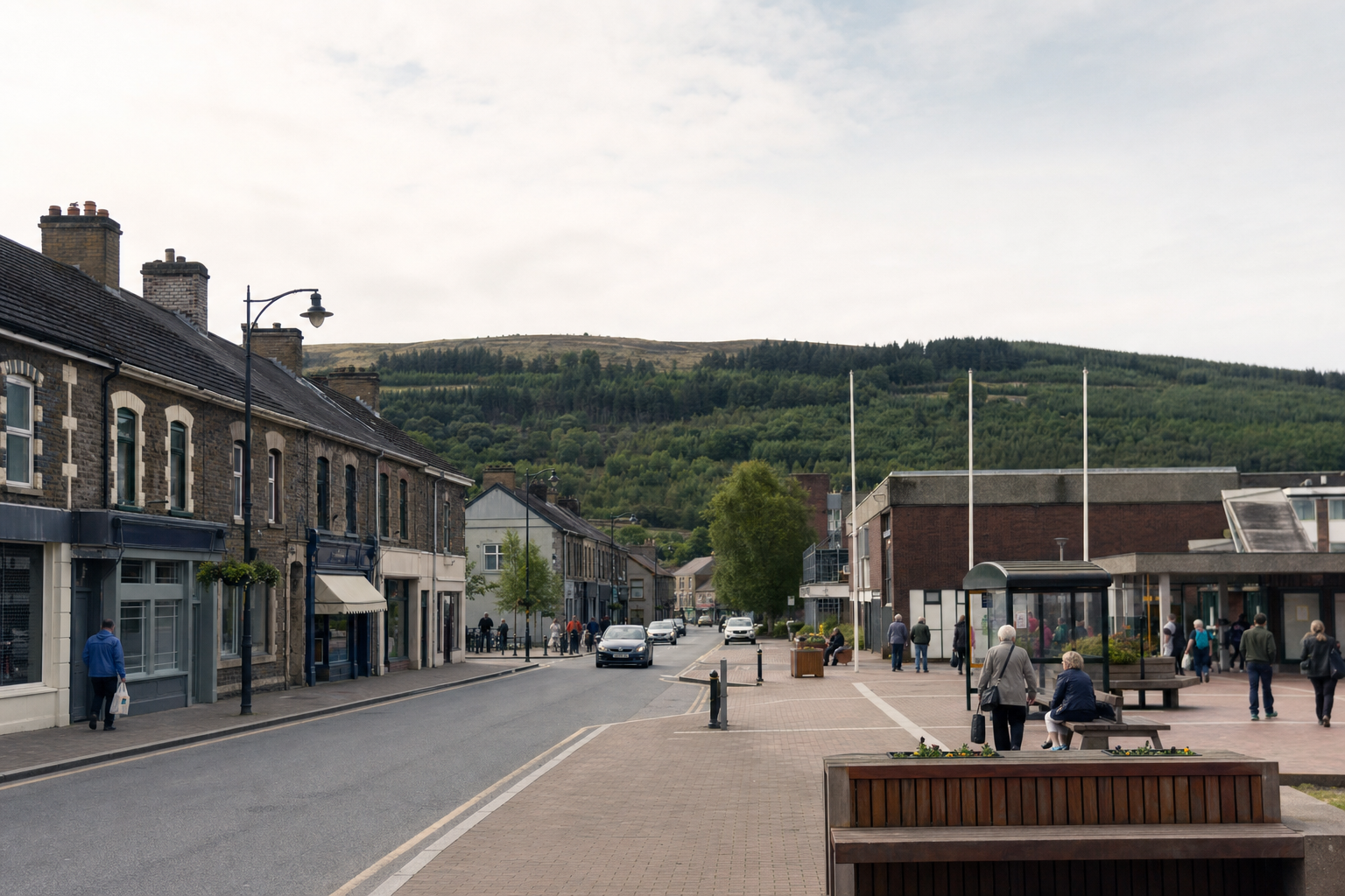 A quiet town street with stone buildings and a backdrop of a green hill, featuring people walking and sitting.