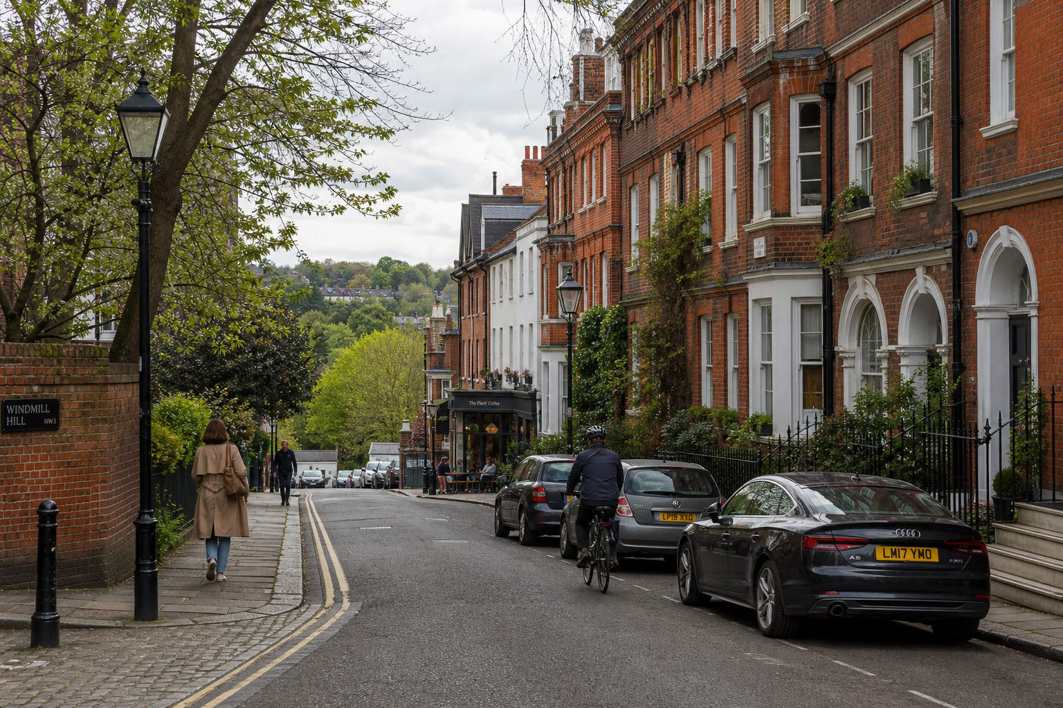 Street in a leafy neighborhood with a cyclist, pedestrians, parked cars, and red brick buildings.