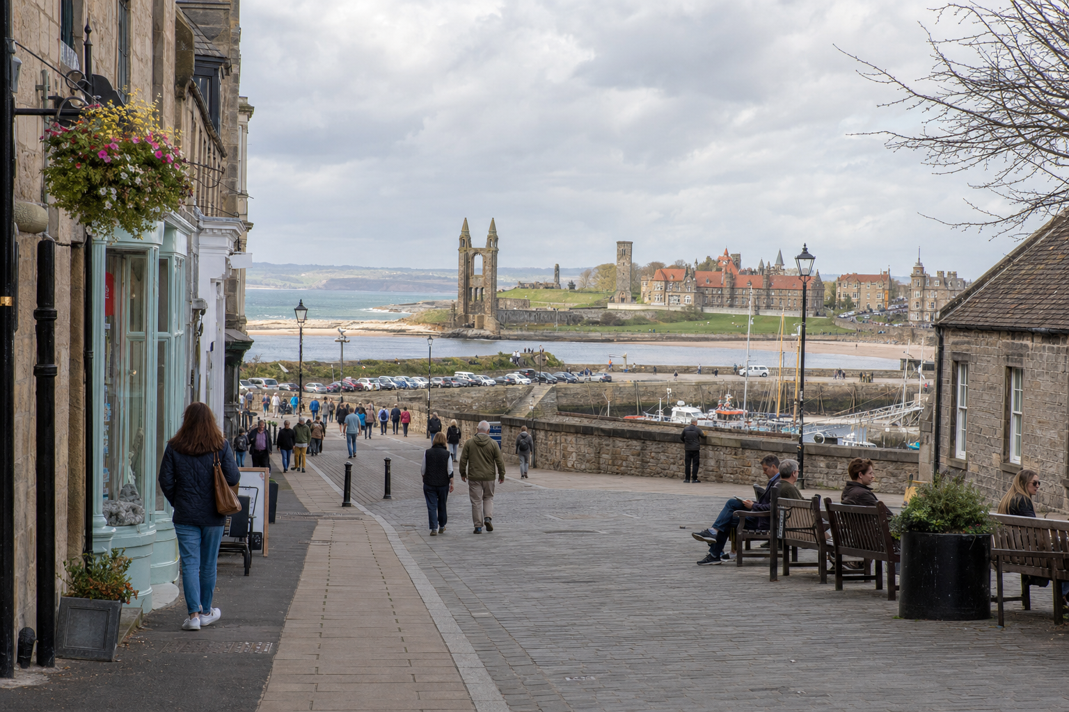 People walking along a cobbled street towards a historic coastal town with ruins and red-roofed buildings by the sea.