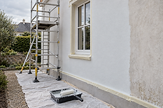 Scaffolding and a paint roller are set up next to a house exterior being painted white.