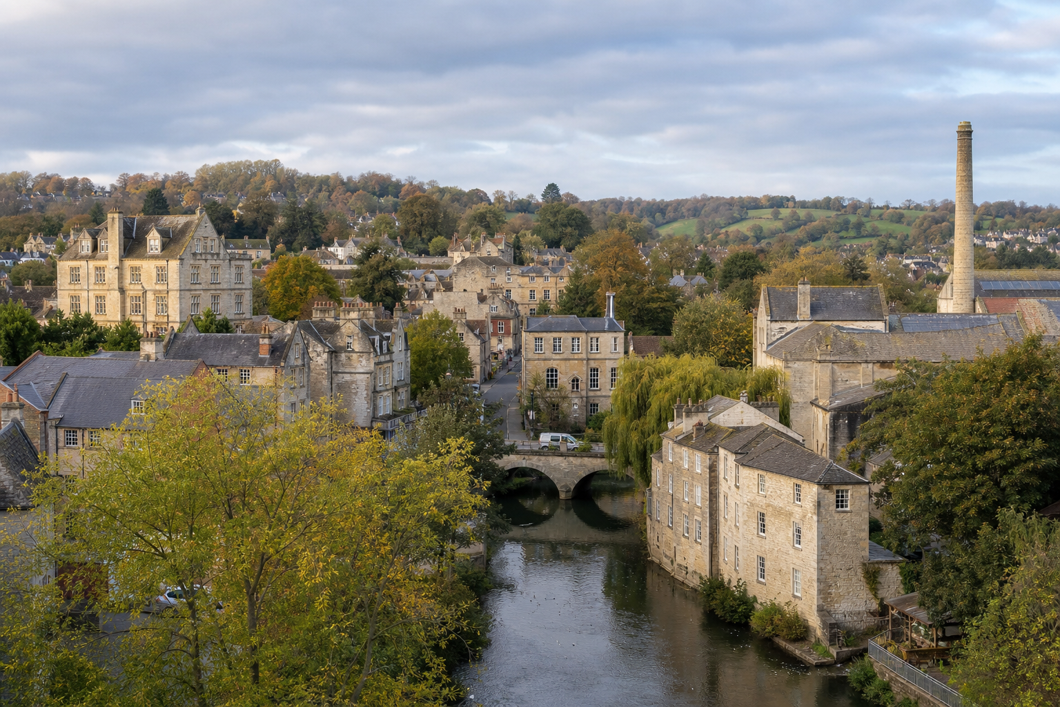 Charming village with historic stone buildings and a river flowing under a bridge, surrounded by lush greenery.