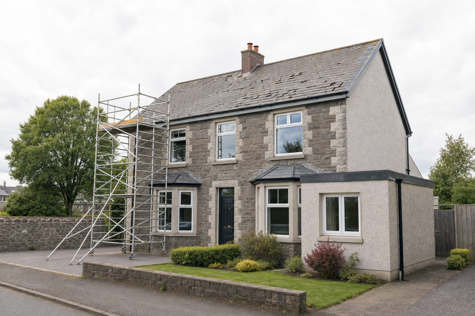 A detached stone house with scaffolding on the side, under overcast skies.
