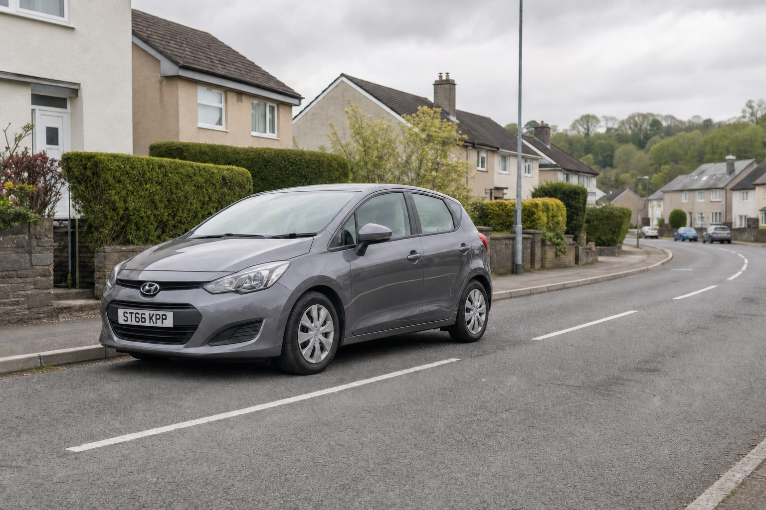 A grey Hyundai car parked on a suburban street with houses and greenery in the background.