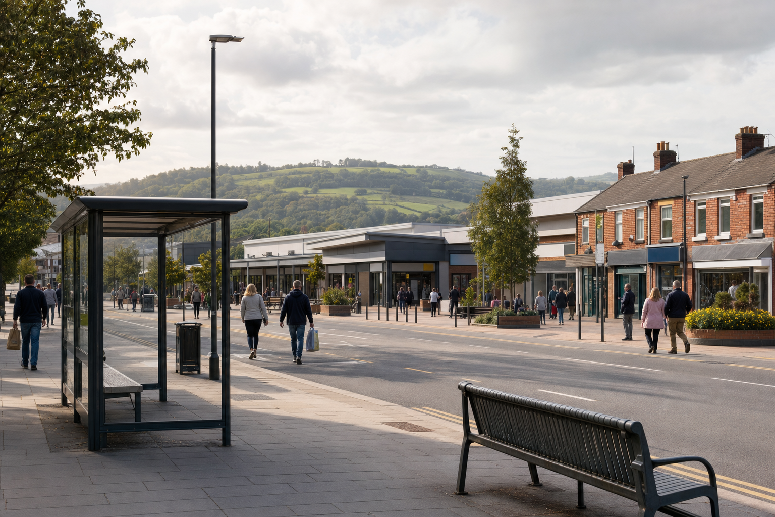 People walking along a pedestrian street lined with shops, set against a backdrop of lush green hills.