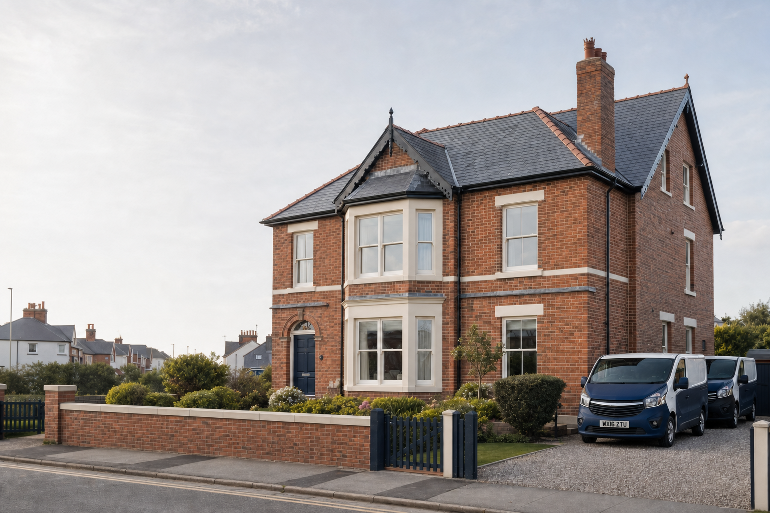 A large red-brick house with blue double doors and two vans parked in the driveway on a residential street.