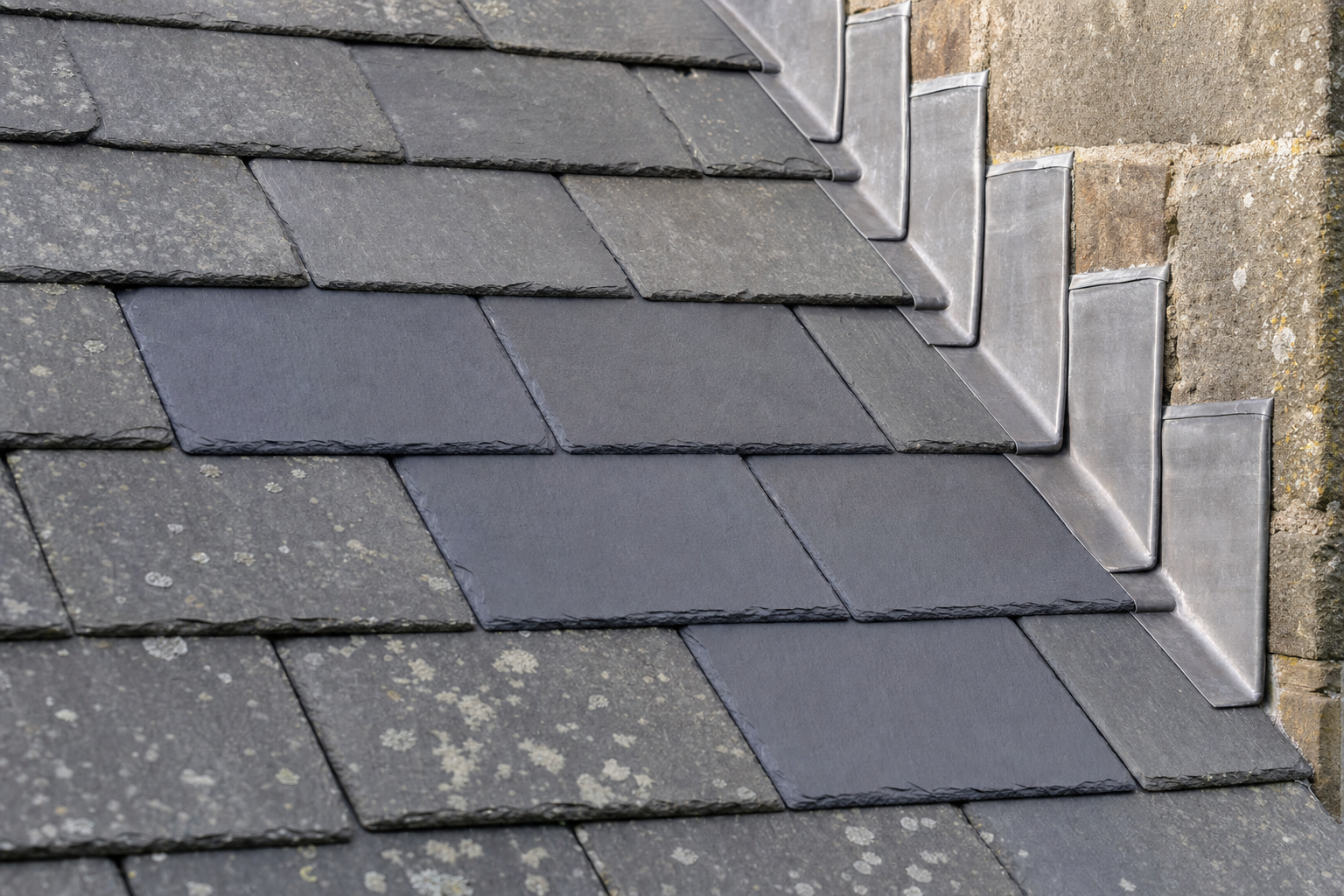 Slate roof with lead flashing next to a stone wall.