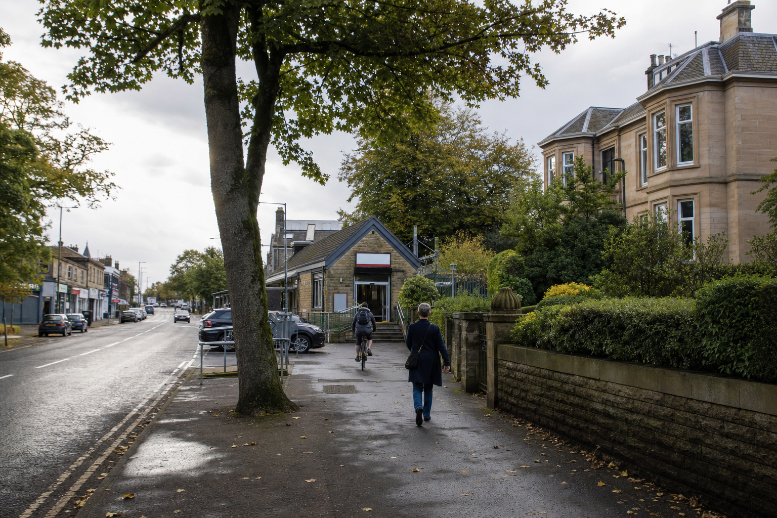 A rainy street scene with a person walking and another cycling past historical buildings and greenery.
