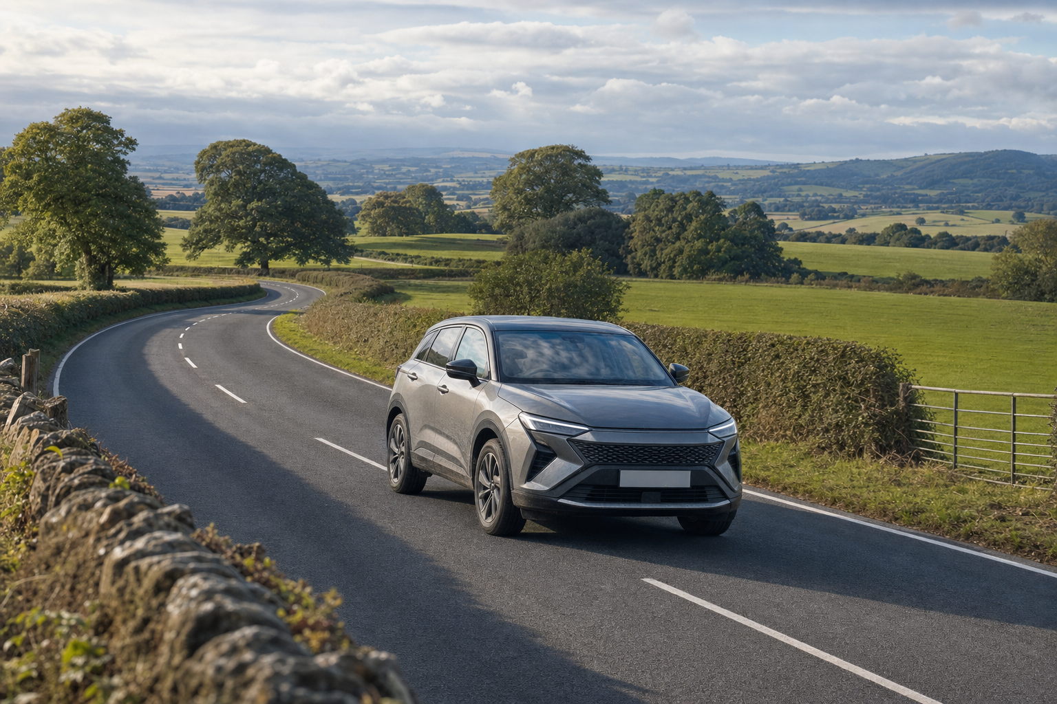 A silver SUV travels along a winding country road bordered by stone walls and lush green fields under a partly cloudy sky.