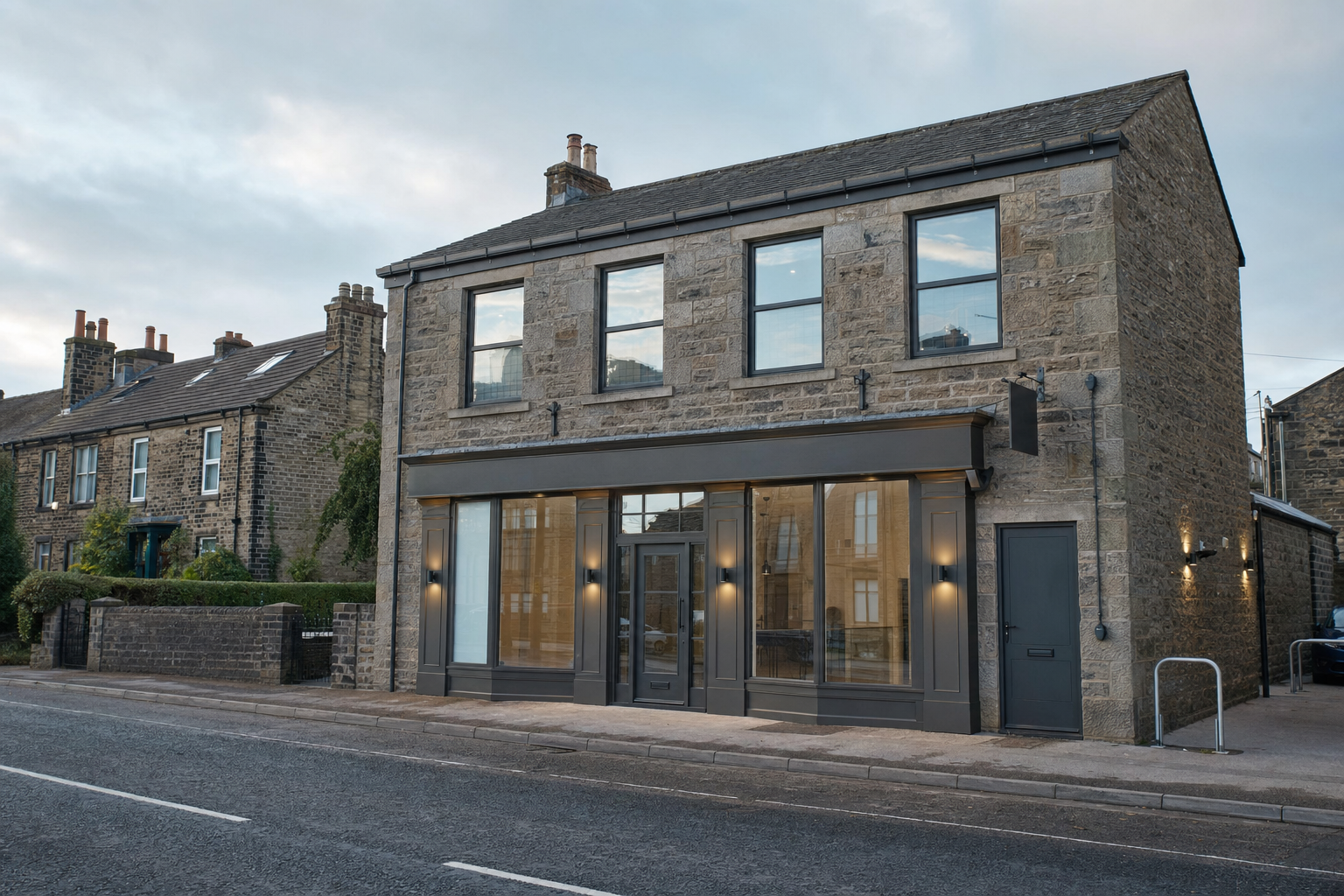 Stone building with large glass windows and doors on a quiet street, surrounded by similar traditional houses.