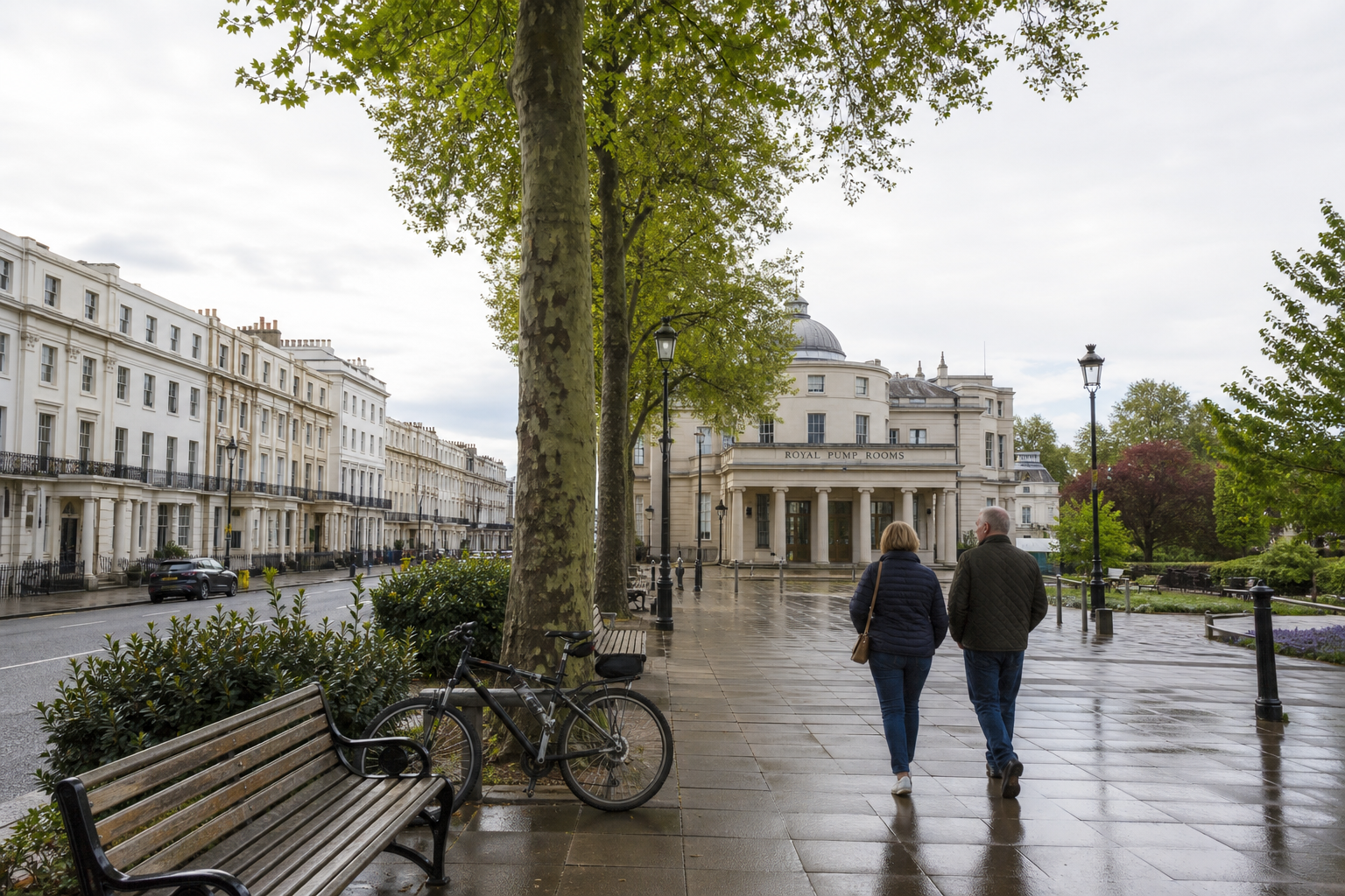 A couple strolls past the Royal Pump Rooms in a tree-lined street with wet pavements and parked bicycle.