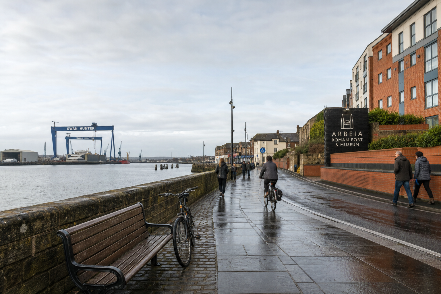 Cyclists and pedestrians on a riverside path near a sign for Arbeia Roman Fort & Museum.