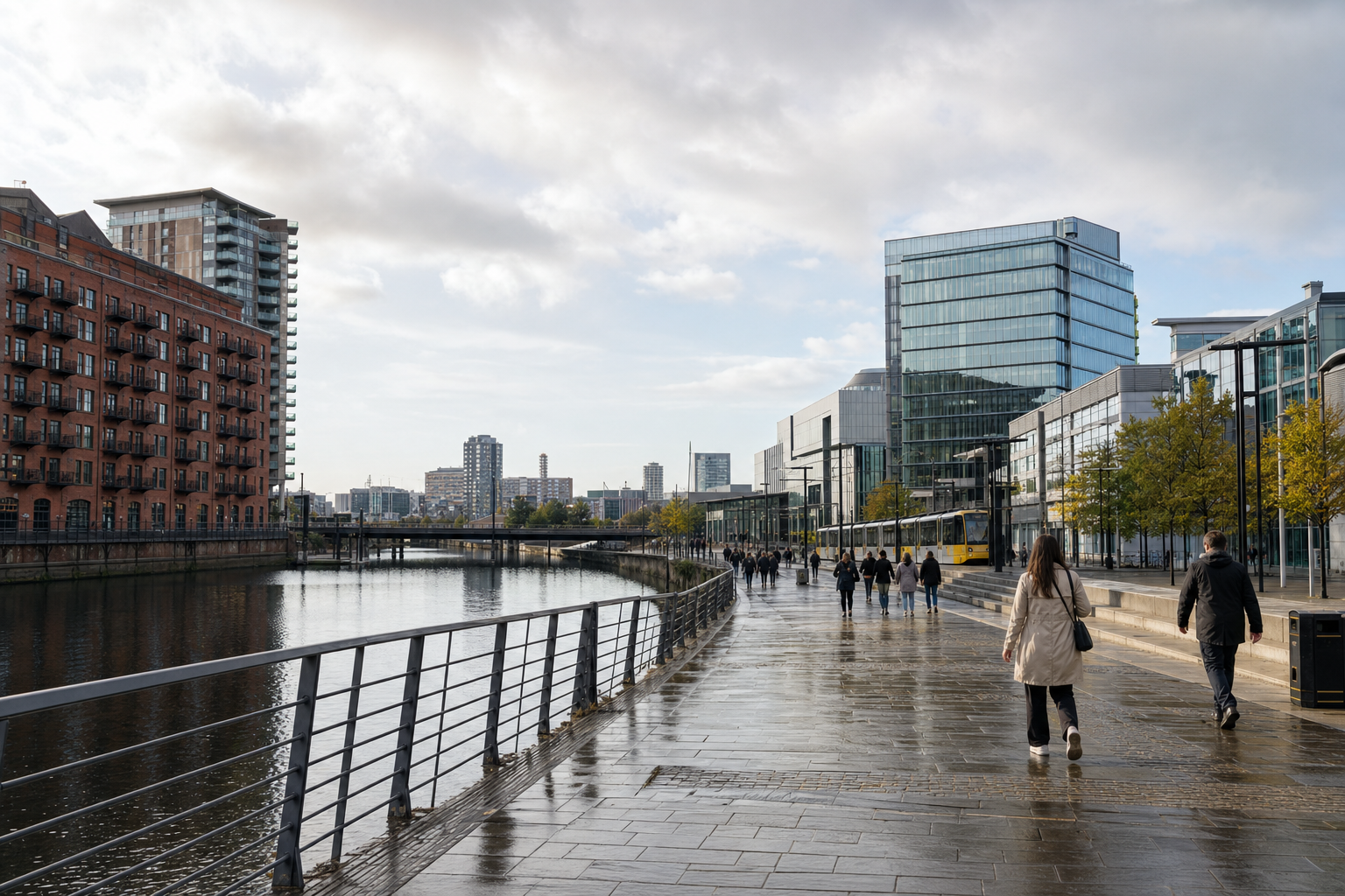 People walking along a modern waterfront promenade with glass buildings and a tram in the background.