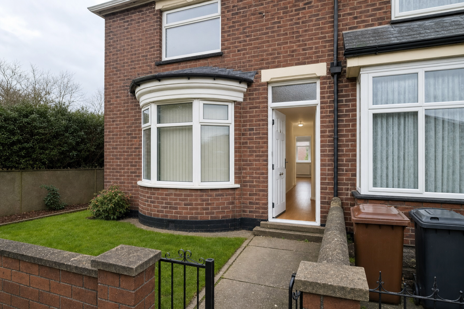 Red-brick semi-detached house with an open white door and a small front garden.