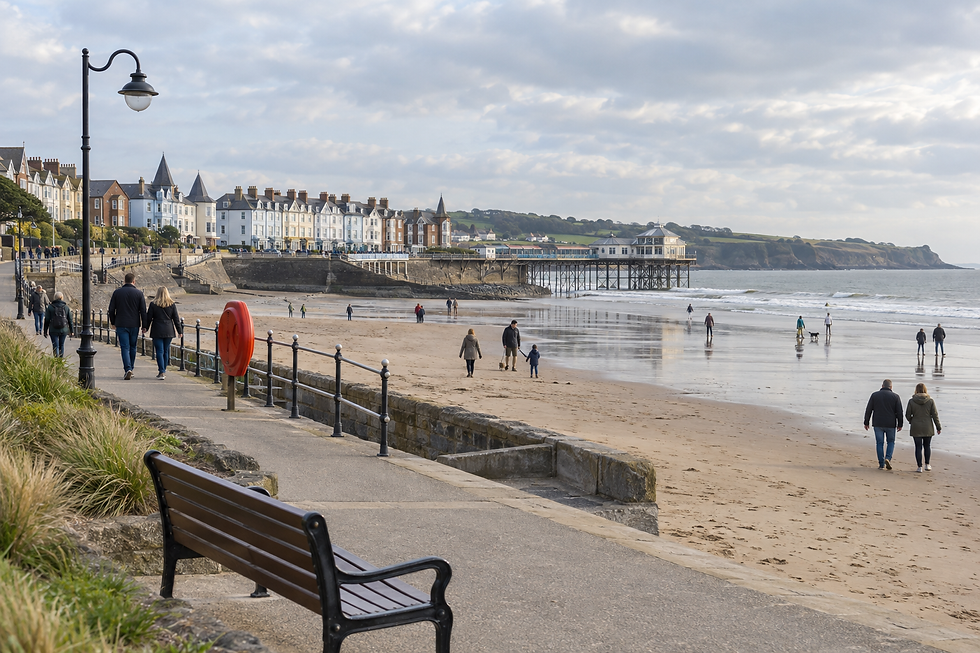 A coastal promenade with Victorian buildings and people walking along the sandy beach and pier.