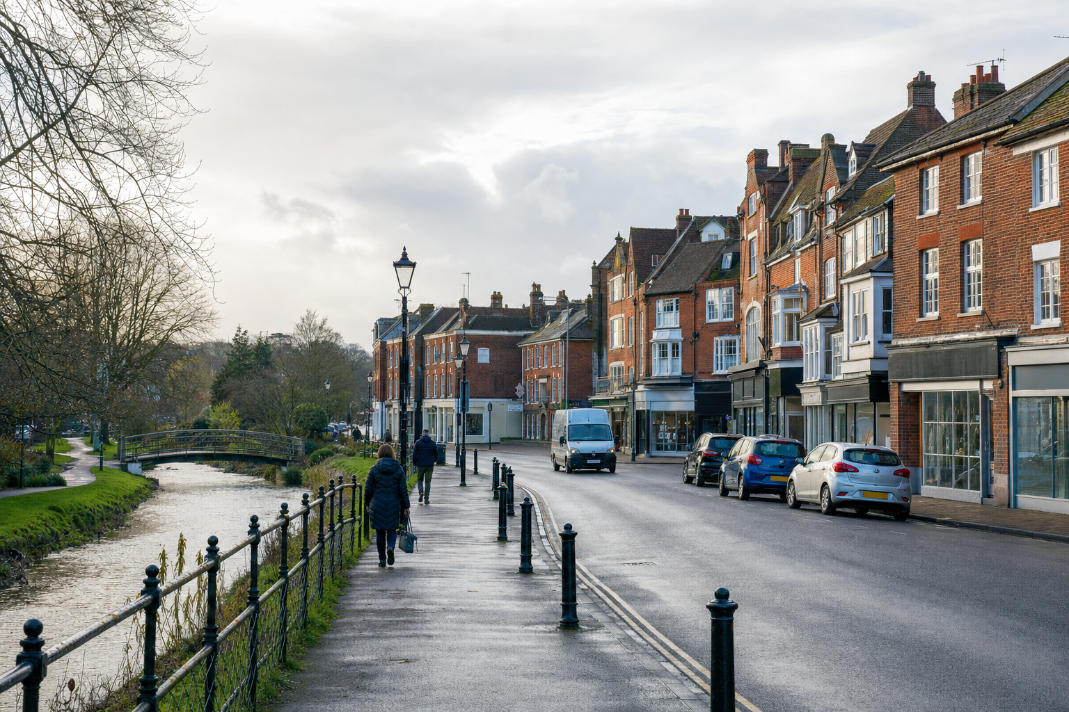 Historic brick buildings line a quiet street alongside a stream and footpath, with pedestrians and parked cars.