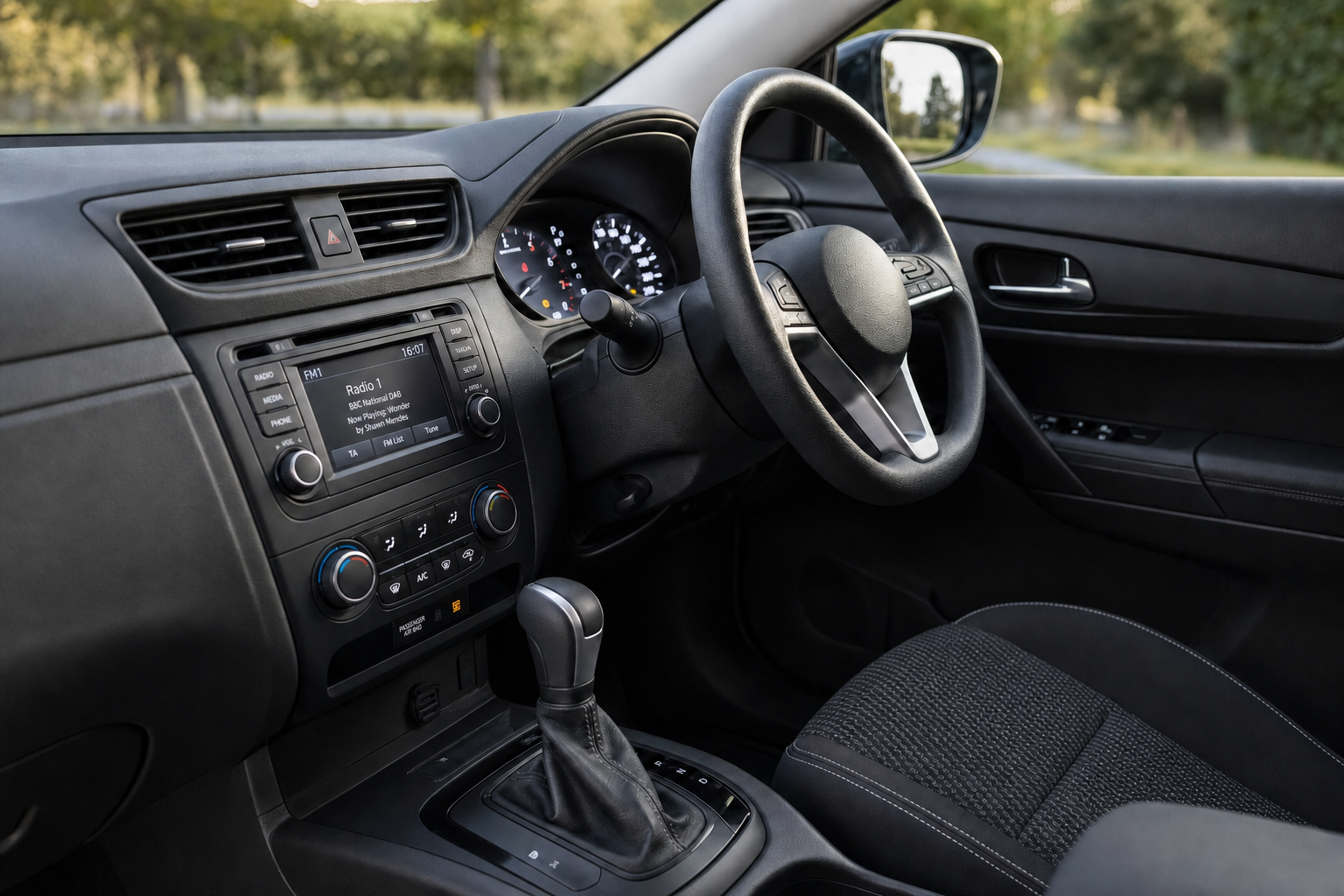 Car interior showing steering wheel, dashboard with radio display, and gear selector on a sunny day.