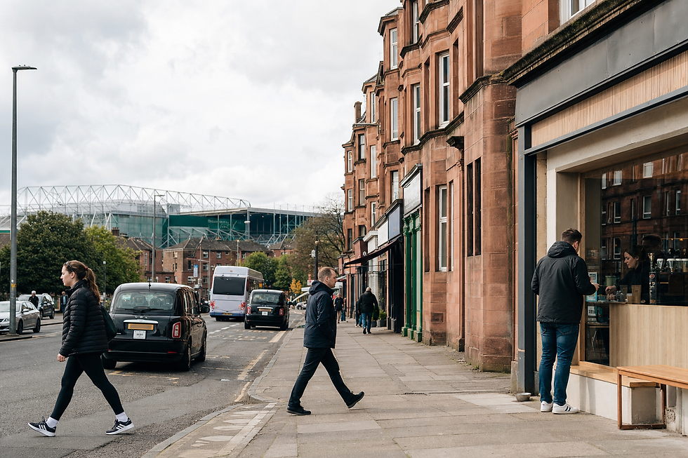 People walking on a street with red brick buildings and a stadium in the background.