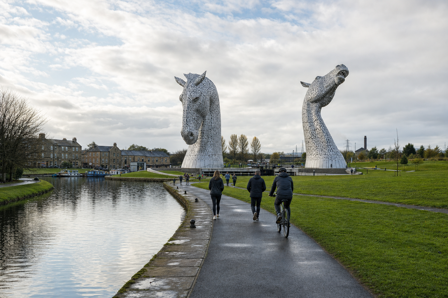 Large horse head sculptures beside a canal path with people walking and cycling nearby.