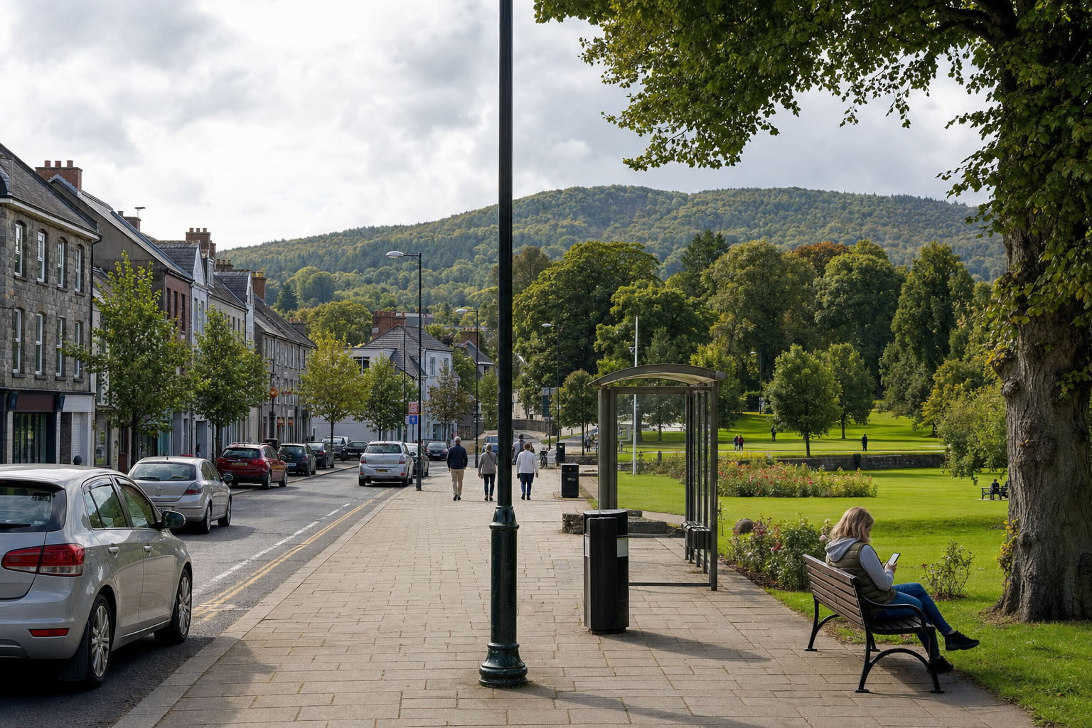A tree-lined street with parked cars, people walking, and a park where a woman sits on a bench using her phone.