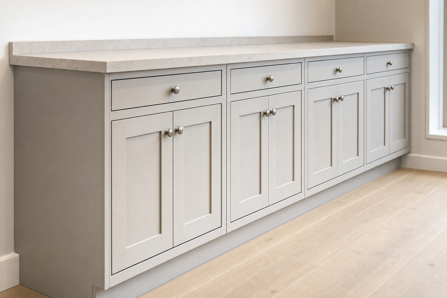 Light grey kitchen cabinets with metal handles and a beige countertop, set on a light wooden floor.