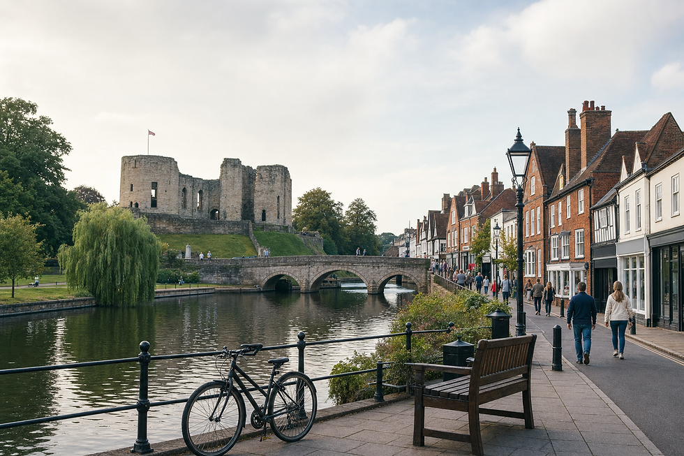 A riverside scene with a historic castle, stone bridge, and people walking along a street lined with traditional buildings.