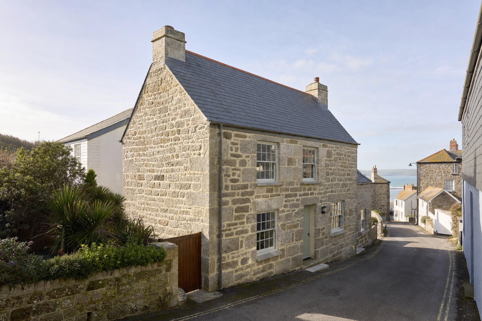 Stone cottage on a narrow street with sea view in the background.