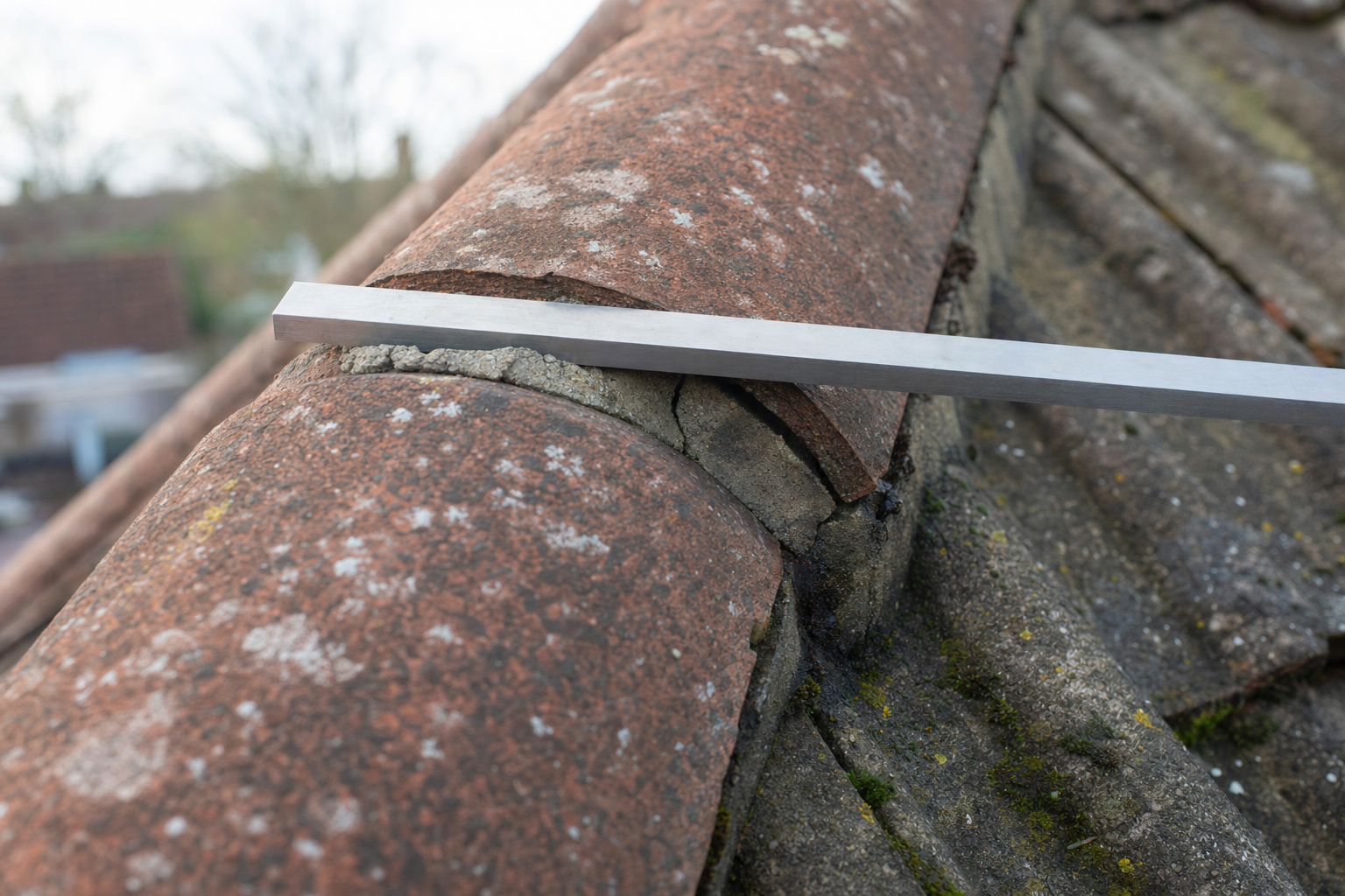 A metal straightedge rests on a cracked roof ridge tile, highlighting damage on the roof.