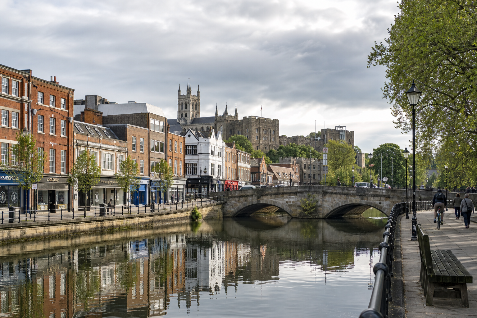 A riverside cityscape with historic buildings, a stone bridge, and reflections on the water under an overcast sky.