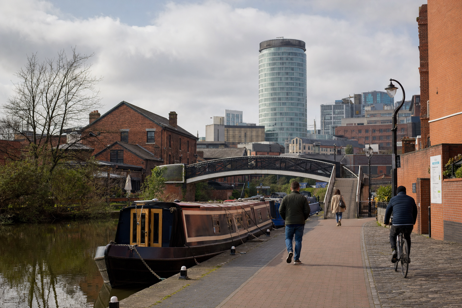 People walking and cycling along a canal towpath with narrowboats and modern buildings in the background.