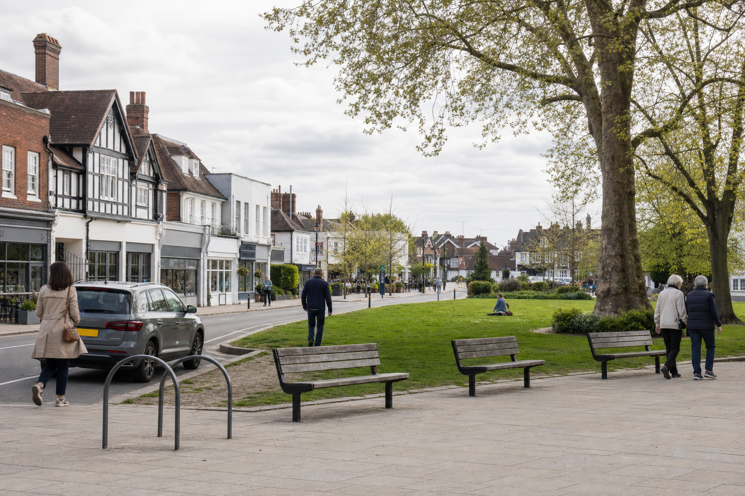 Street view of a British town with people walking by a park and traditional buildings in the background.