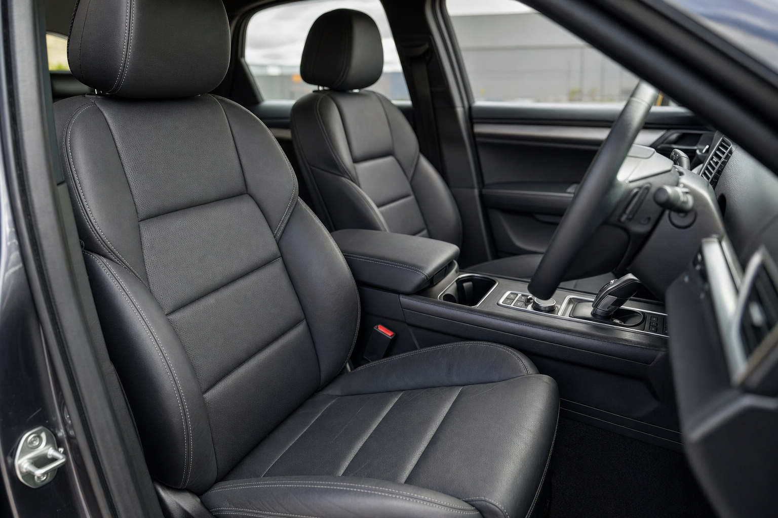 The interior of a modern car with black leather seats, a central console, and a steering wheel is shown.