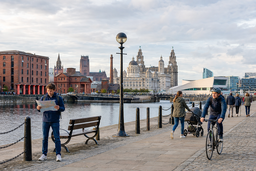 A man reads a map by the waterfront in Liverpool, with people walking and cycling along the promenade.