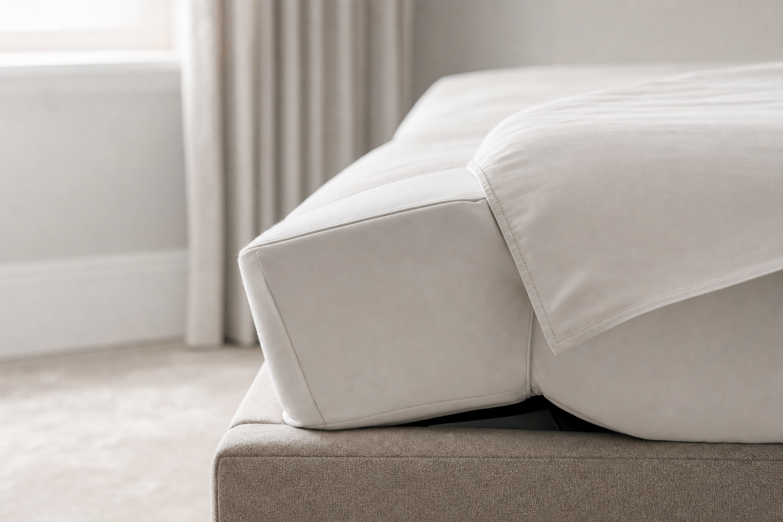 Close-up of a neatly made bed with white linens and a beige headboard.