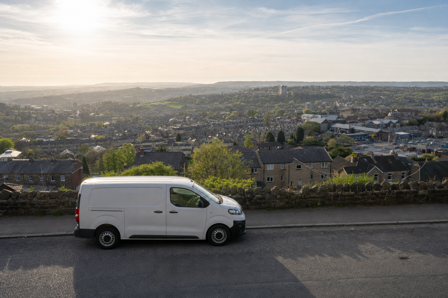 White van parked on a hill overlooking a townscape under a hazy sky.