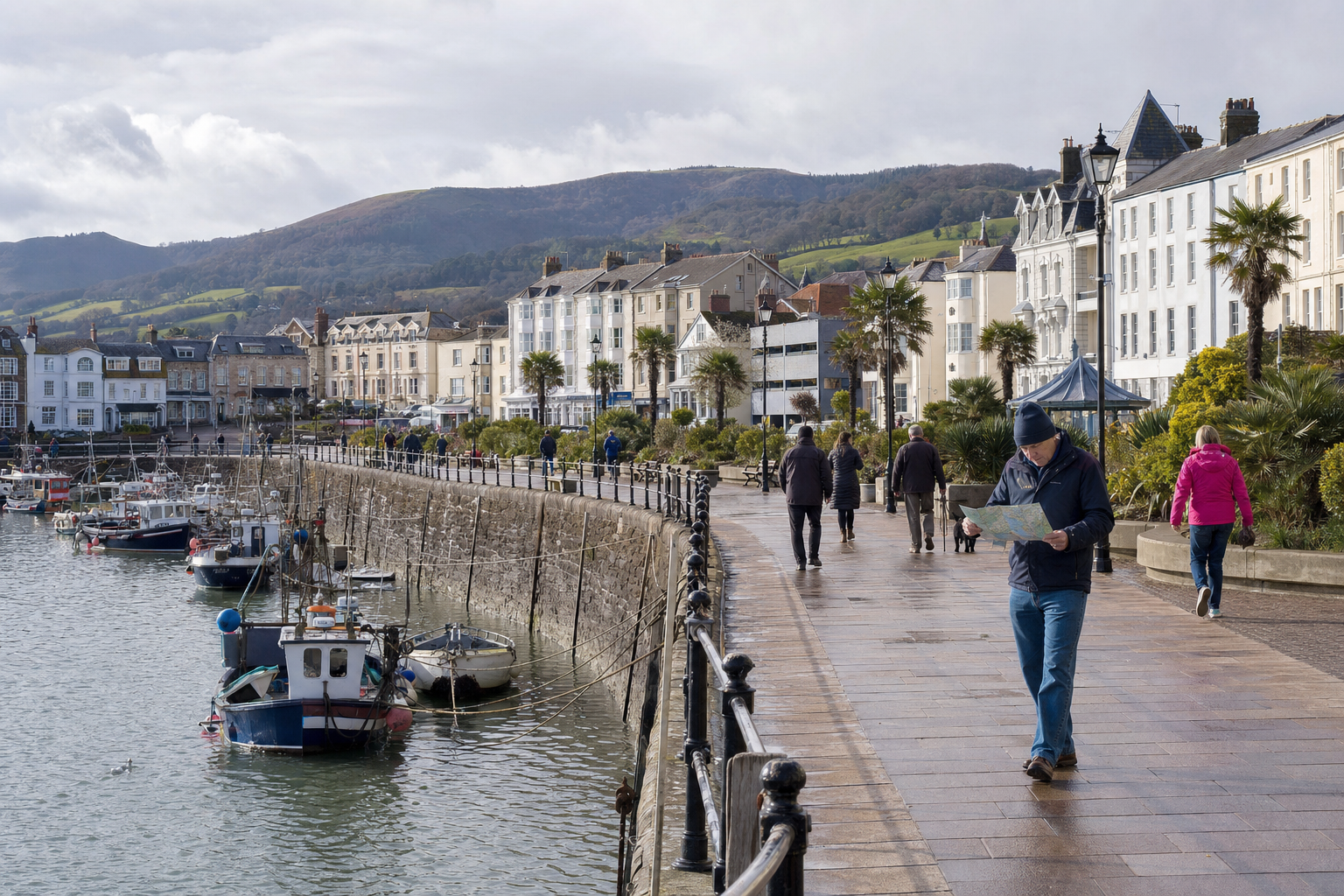 A man reads a map while walking along a seafront promenade with boats and Victorian buildings in the background.