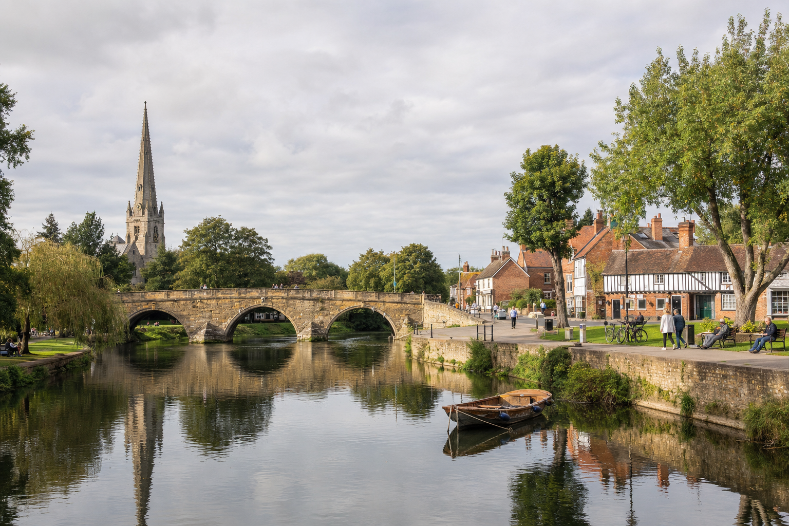 A serene riverside scene with a stone arched bridge, a church spire, and quaint buildings reflecting in the water.