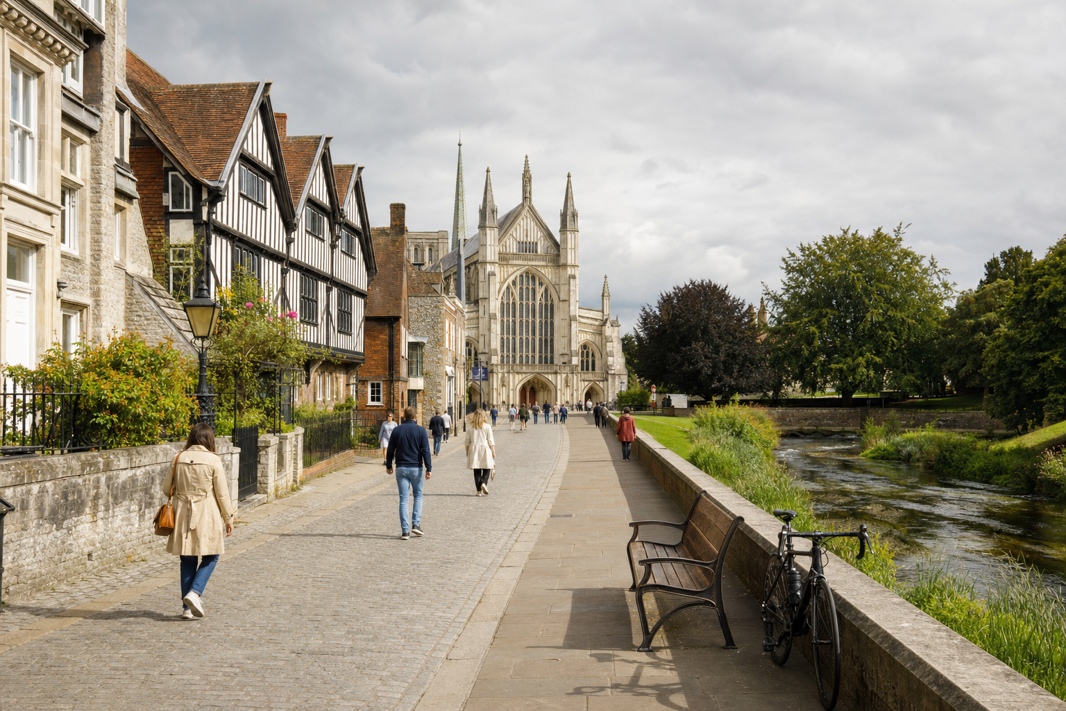 People walking towards a historic cathedral along a cobblestone street beside a river and traditional buildings.