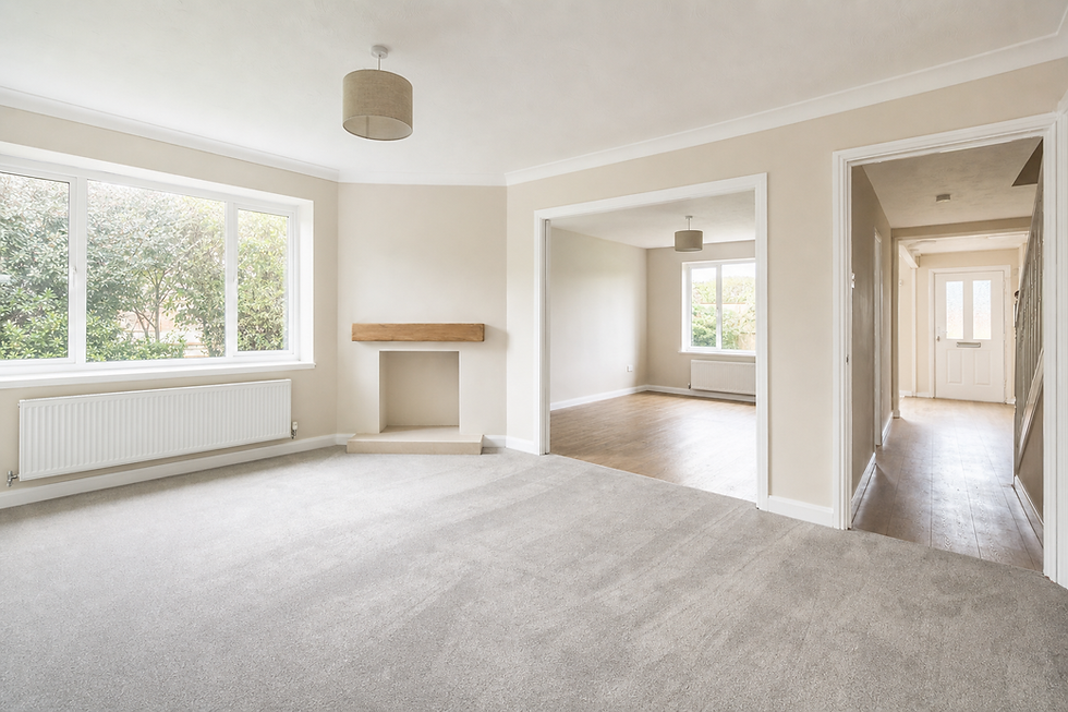 Spacious, empty living room with beige walls, grey carpet, large window, and adjacent hallway leading to another room with