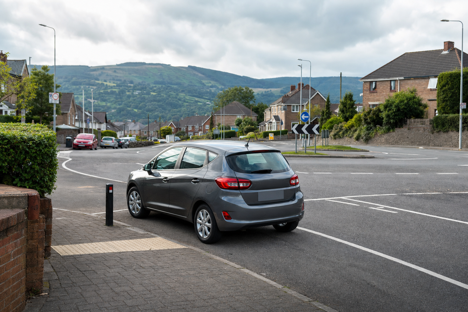 Grey hatchback parked near a residential roundabout with green hills in the background.