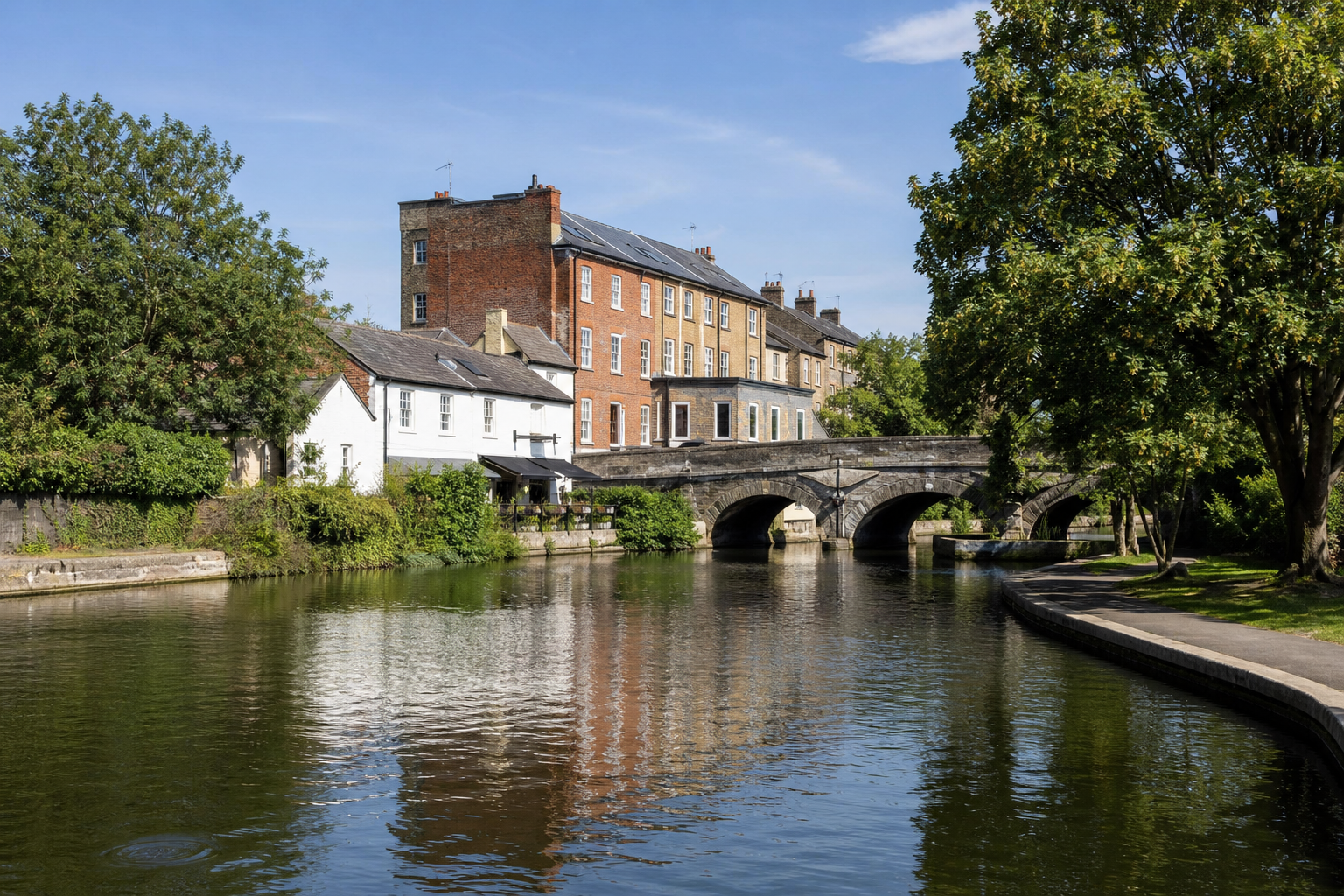 Historic buildings and a stone bridge over a river in a scenic, tree-lined setting.