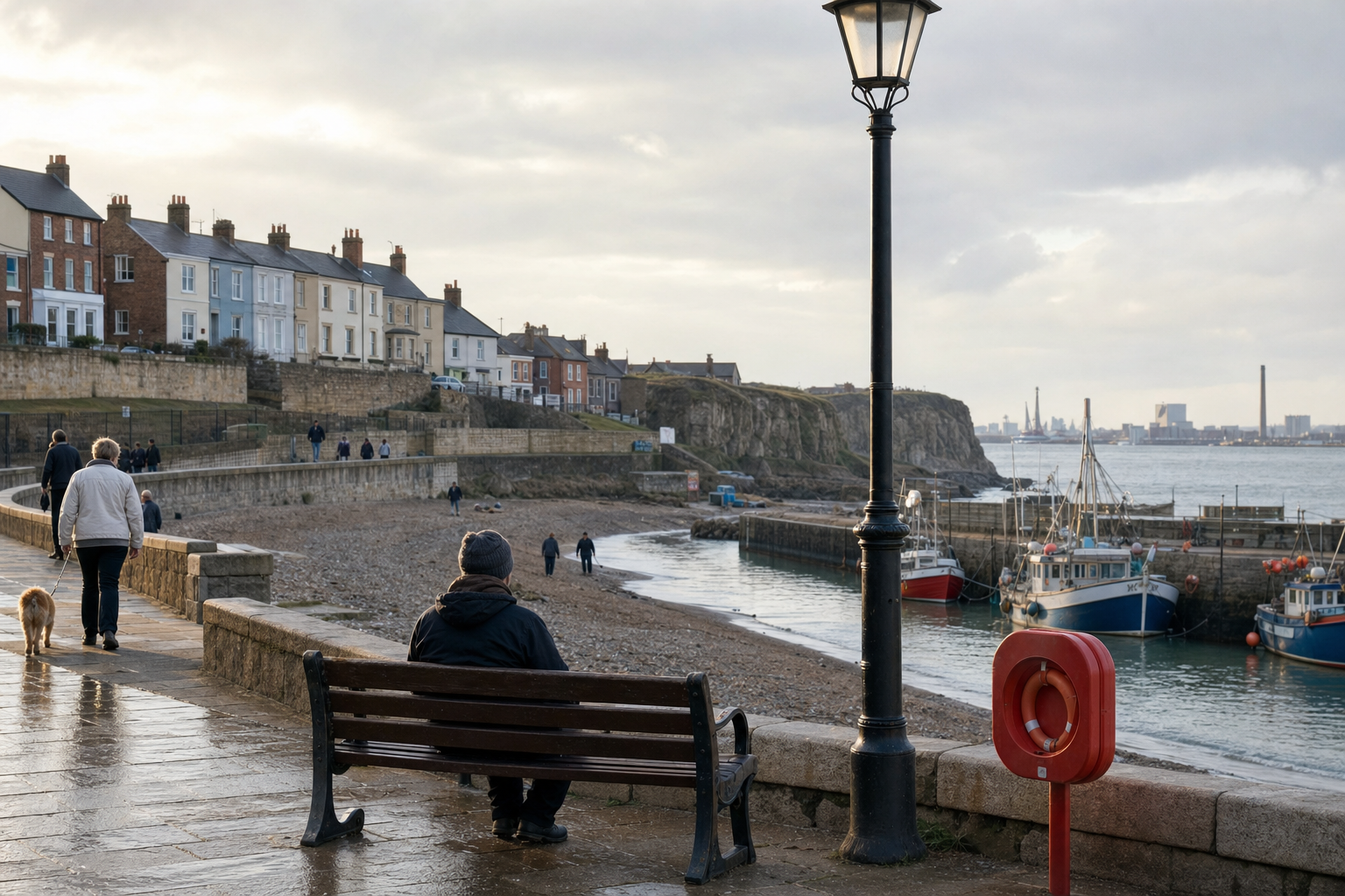 Seaside promenade with people walking, a person sitting on a bench, and boats docked by a harbour.