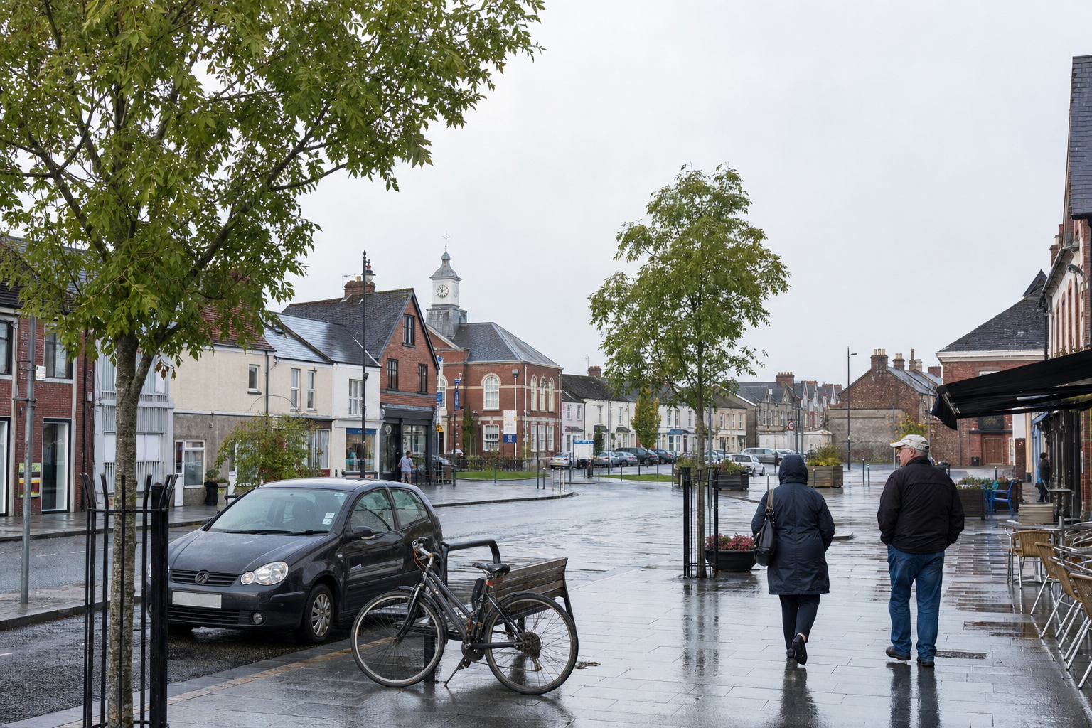 Two people walking on a wet street lined with buildings and trees, with a parked bicycle and car nearby.