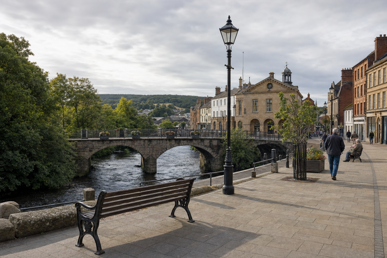 Stone bridge over a river with people walking on a promenade, surrounded by historical buildings and greenery.