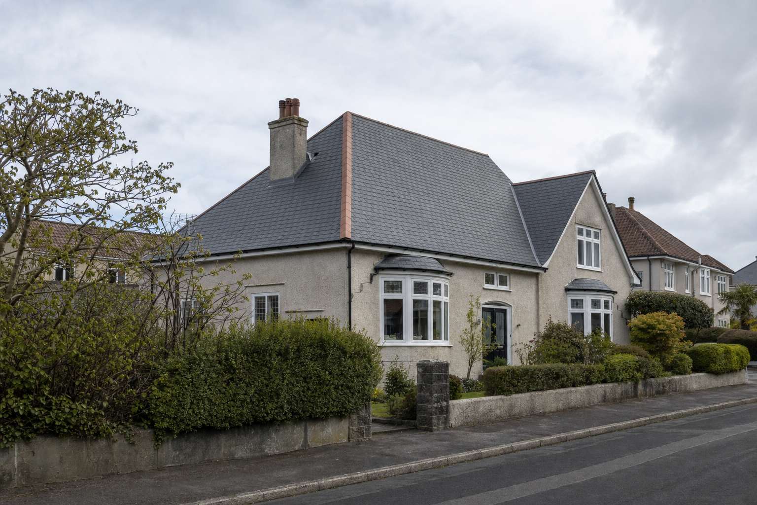 A traditional British house with a slate roof and well-kept garden on a cloudy day.