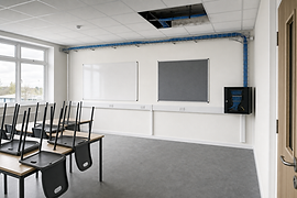 Empty classroom with stacked chairs, whiteboards, and visible blue cable trays overhead