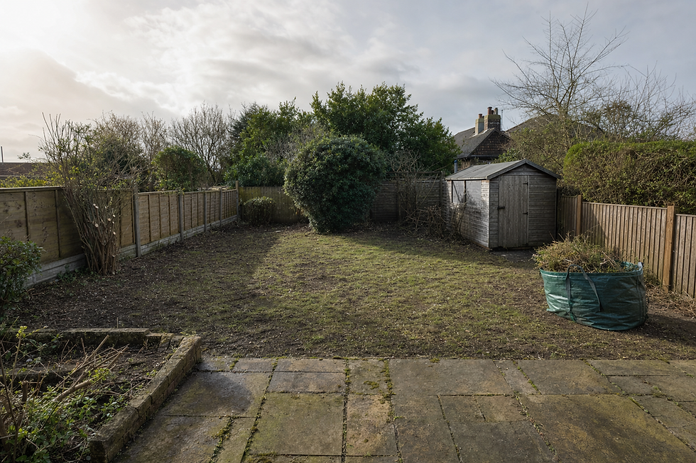 A tidy, fenced garden with a small wooden shed and a bag of garden waste on a partly cloudy day.
