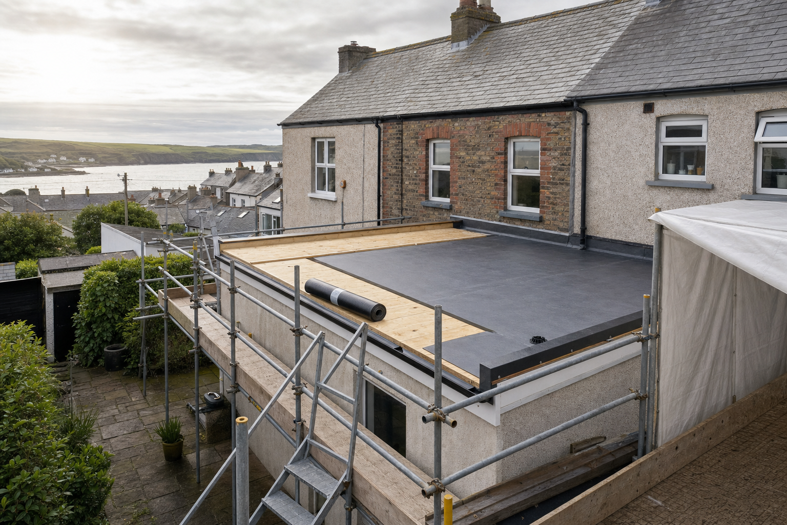 A flat roof installation on a two-storey house with scaffolding and a coastal view in the background.