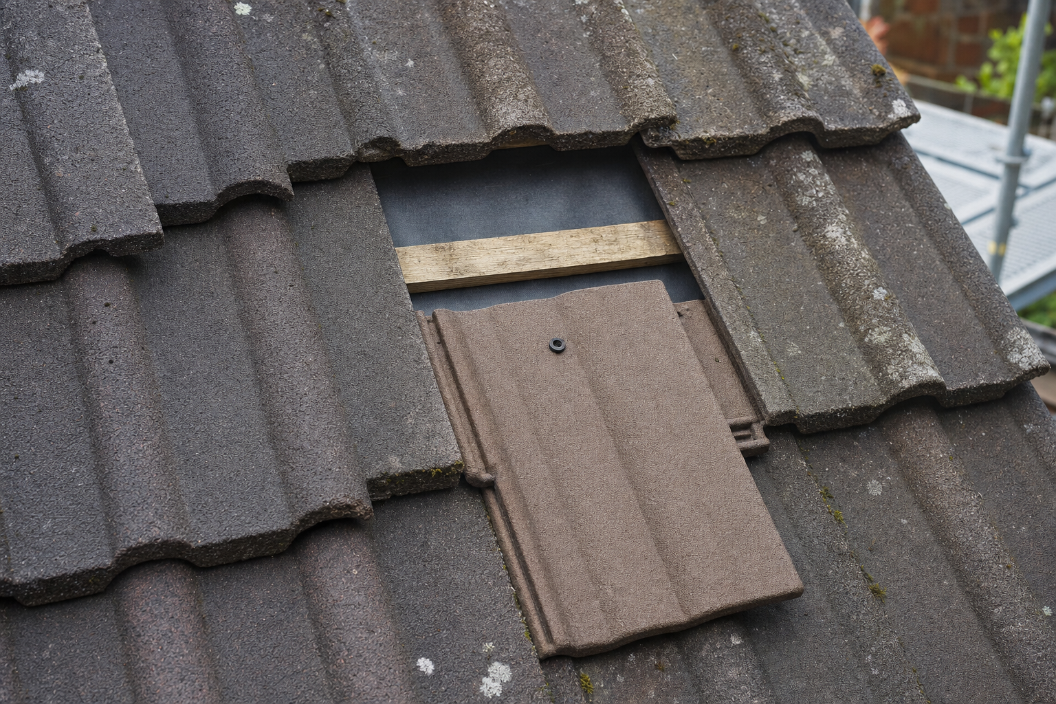 A damaged roof tile has been removed, revealing the wooden support beams beneath.